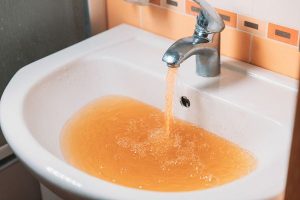 A sink filling up with brown water from the tap.